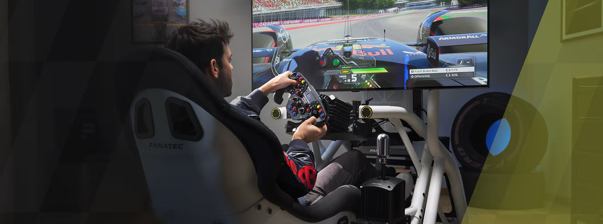 Driver in a Fanatec seat holding a sim racing wheel in front of a large monitor.