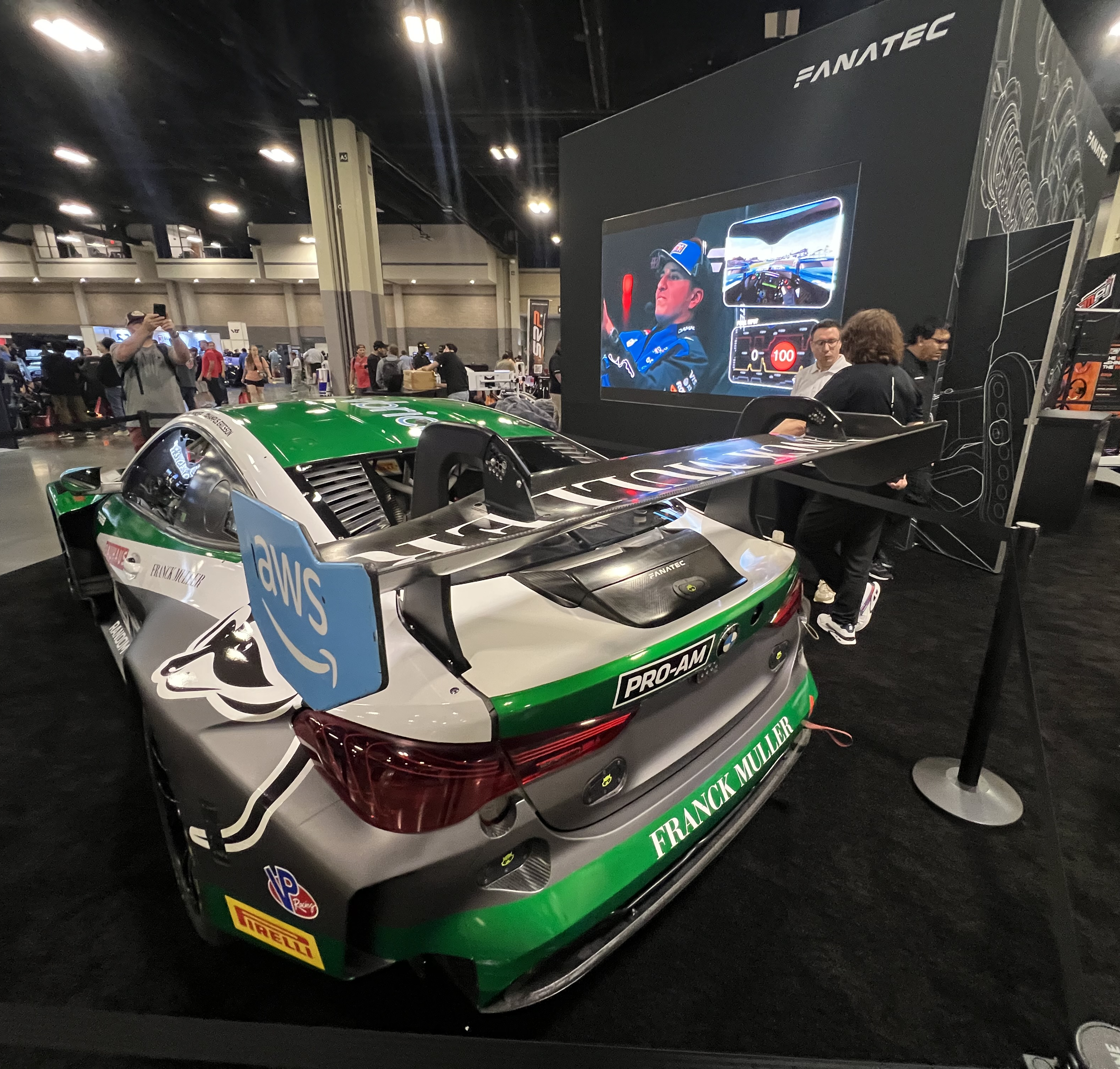 Green and silver GT car on display beside a Fanatec sim racing screen.